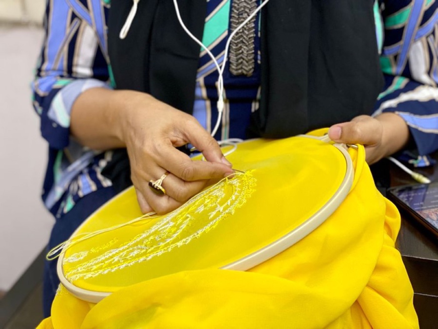 An artisan's hands working fine gold thread into chiffon held in an embroidery hoop